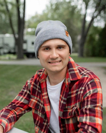 Person wearing a red plaid jacket and gray beanie outdoors with trees in the background