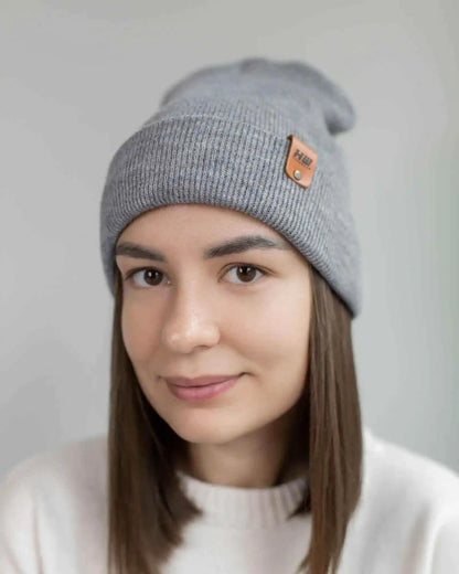Person wearing a gray beanie with a brand logo on a plain background