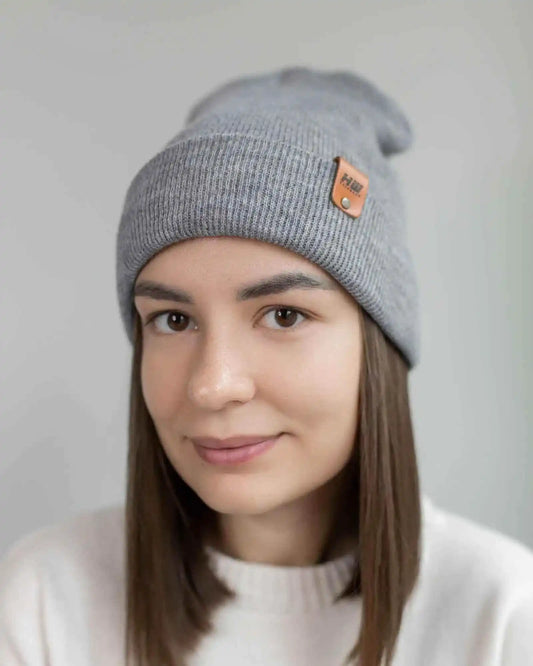 Person wearing a gray beanie with a brand logo on a plain background