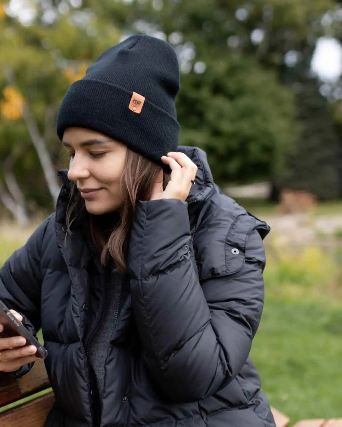Person wearing a black beanie with a logo and a black puffer jacket outdoors.
