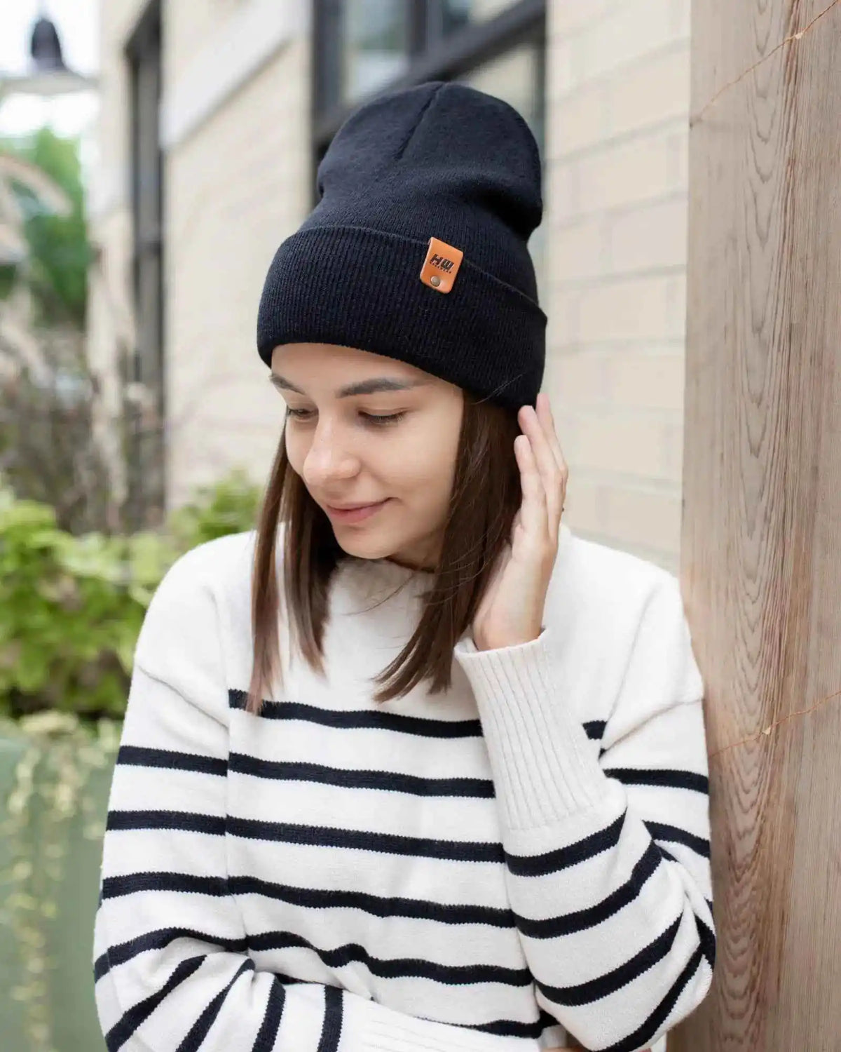 Woman wearing a black beanie with a brand logo and a striped sweater outdoors.