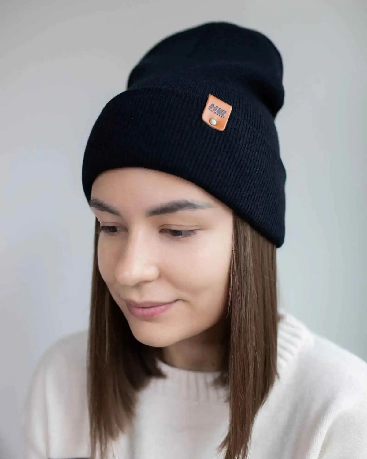 Person wearing a black beanie with a brand logo on a plain background