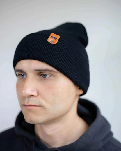 Person wearing a black beanie with an orange logo against a plain background