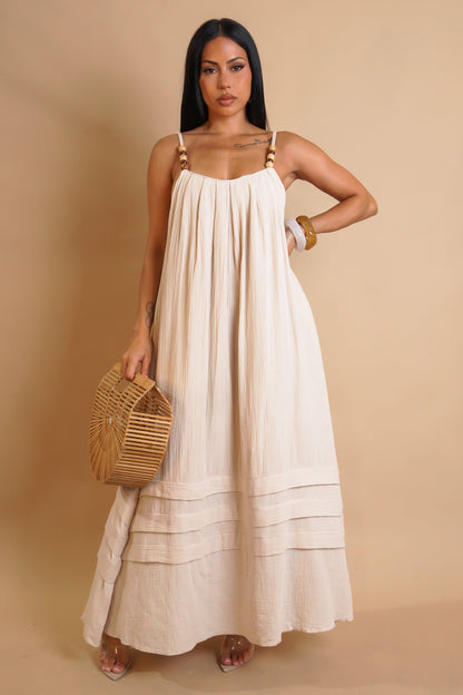 Woman wearing a beige dress holding a woven bag against a beige background