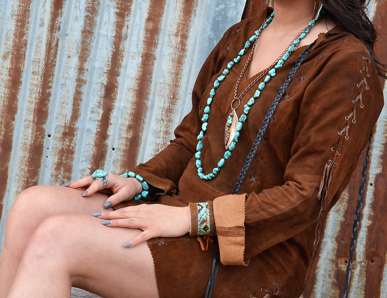 Person wearing a brown outfit with turquoise jewelry against a rustic metal background
