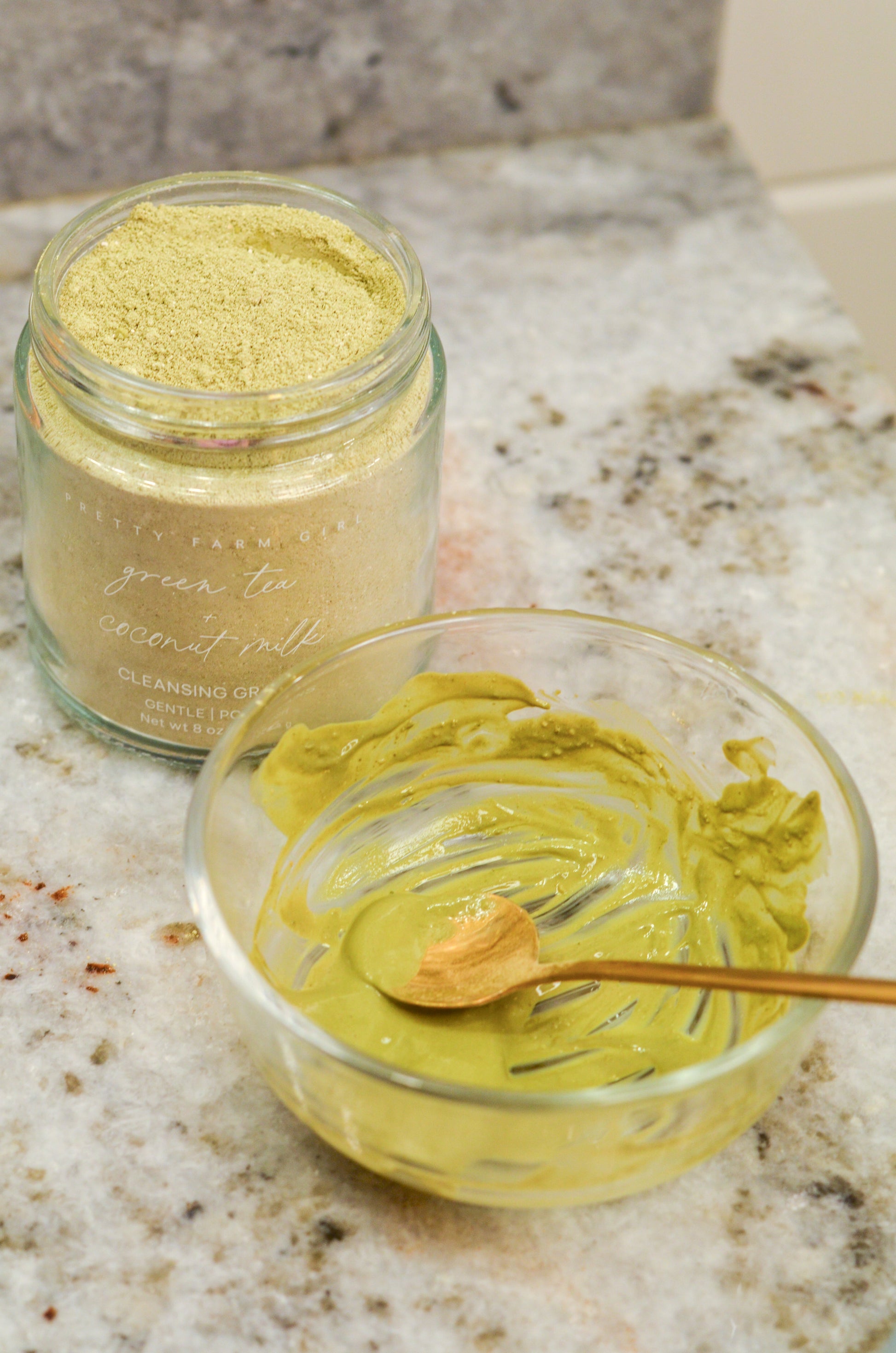 Jar of green tea ceremonially harvested powder on a marble surface with a small bowl of green tea powder.