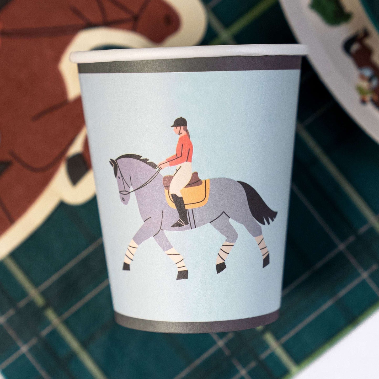 Paper cup with a horse and rider illustration on a checkered surface