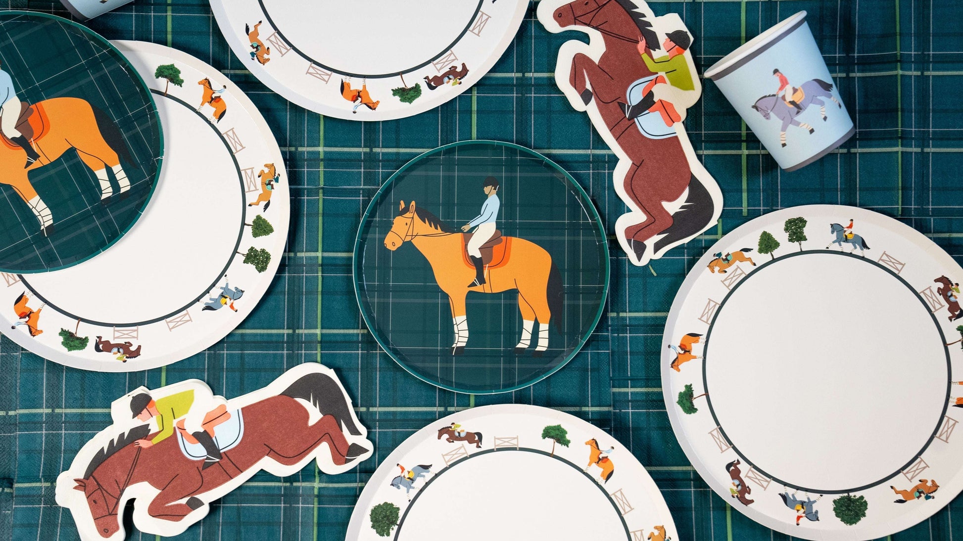 Assorted horse-themed paper plates, napkins, and a cup with equestrian illustrations on a green plaid fabric background.