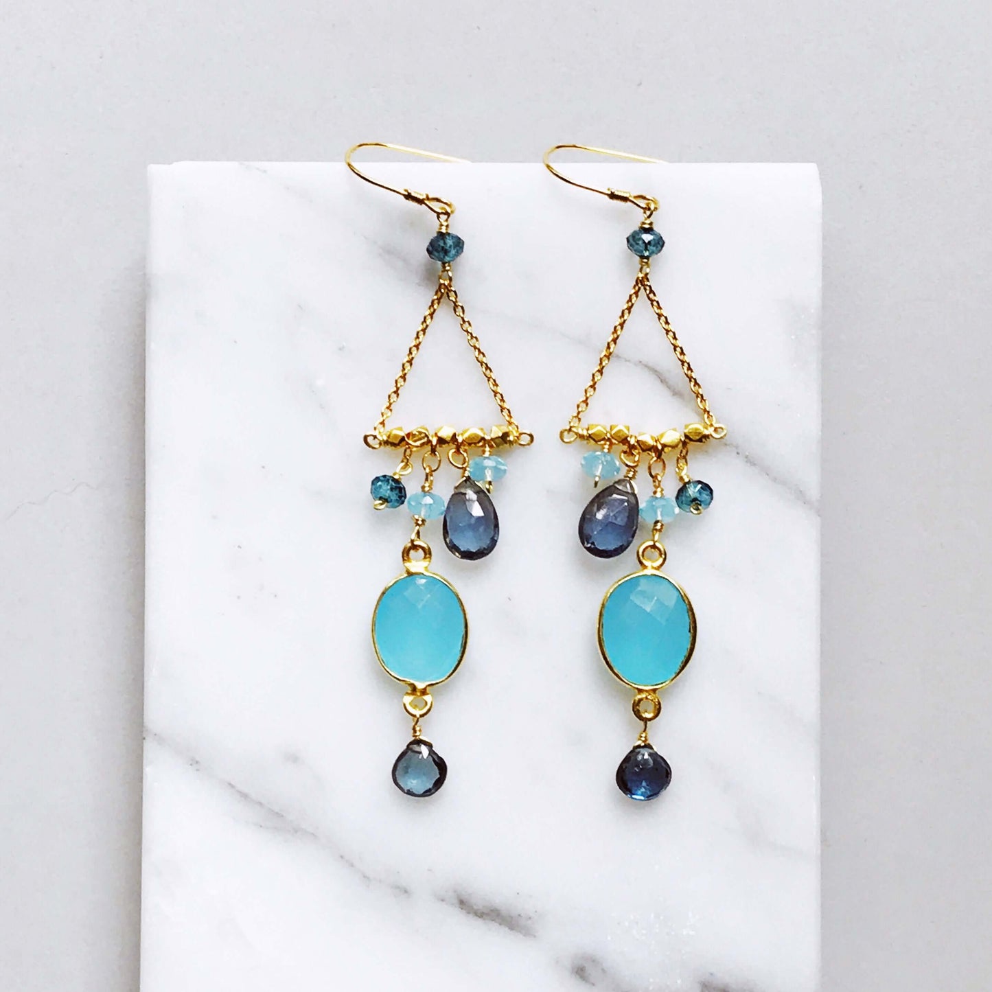 Gold earrings with blue and black gemstones on a white marble surface