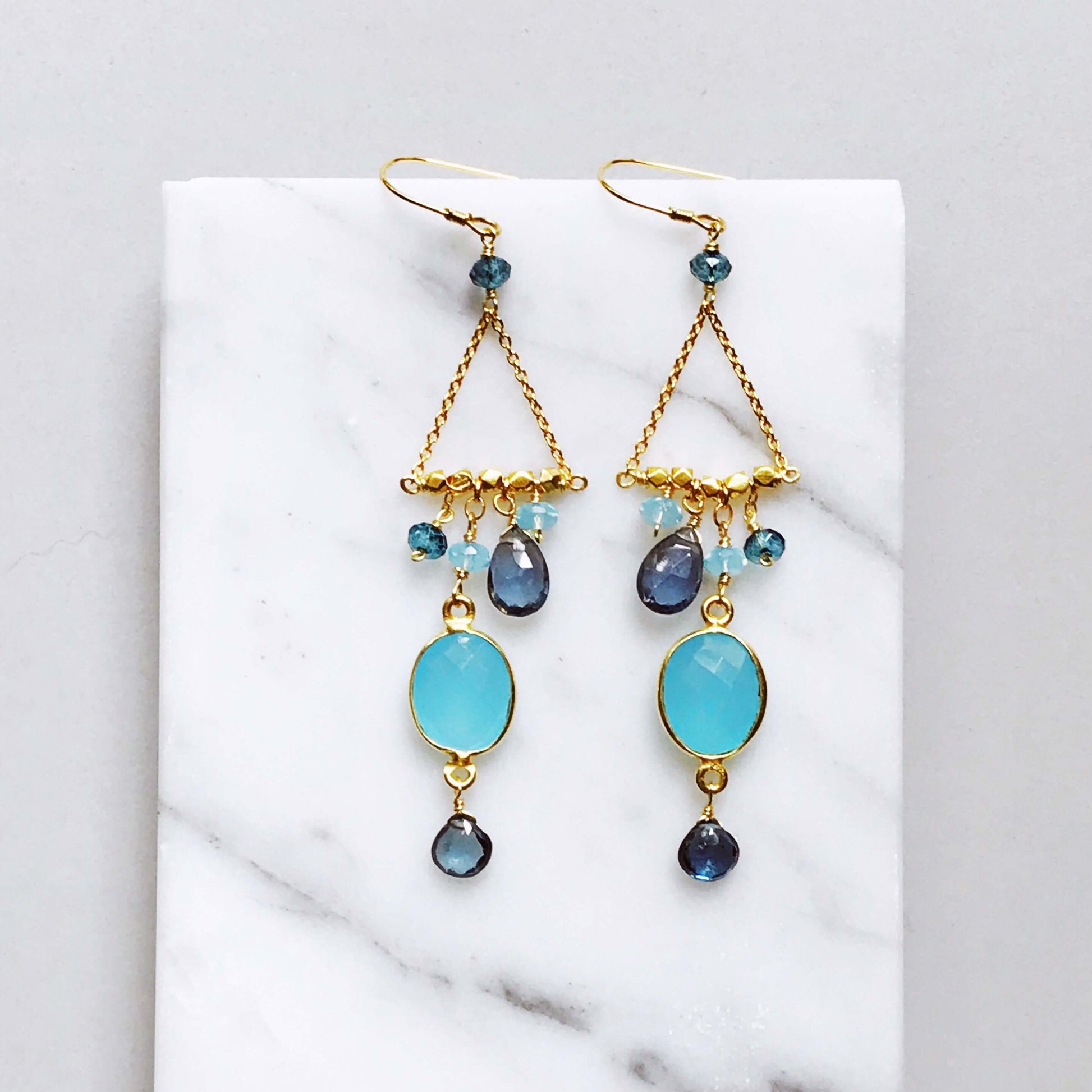 Gold earrings with blue and black gemstones on a white marble surface