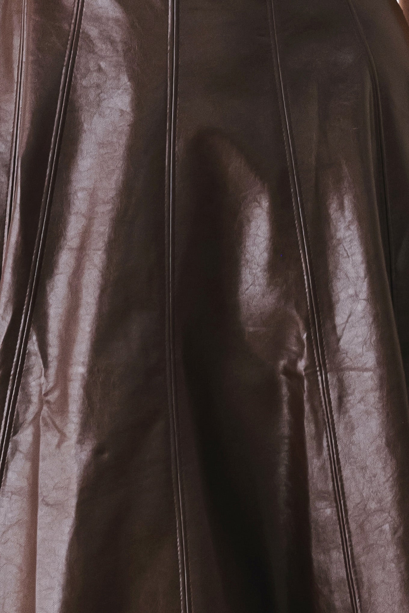 Close-up of a dark brown leather garment with vertical seam detailing and a glossy finish.