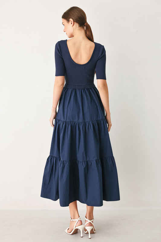 Rear view of a navy blue midi dress with a ribbed knit bodice, scoop back, short sleeves, and a tiered fabric skirt.