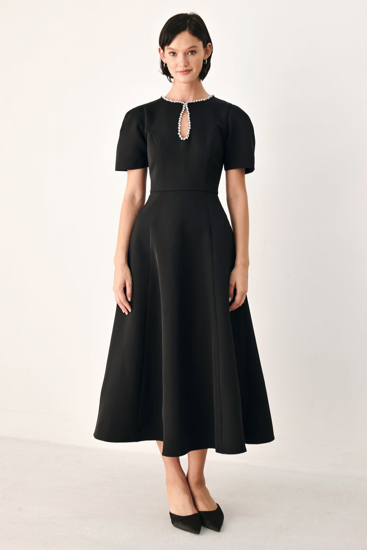 Model wearing the black After Dark Elegance midi dress with a jeweled keyhole neckline, short puff sleeves and a flared skirt.