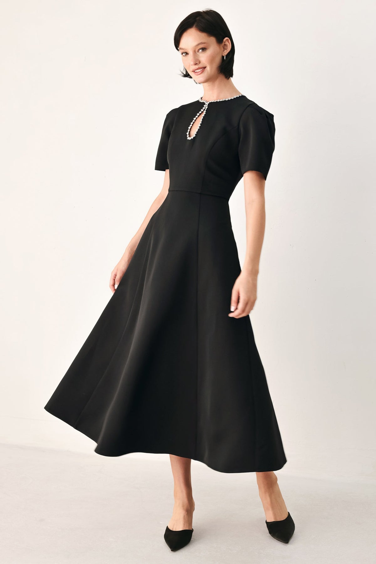 Angled front view of the black jeweled midi dress showing its fitted waist and flowing circle skirt.