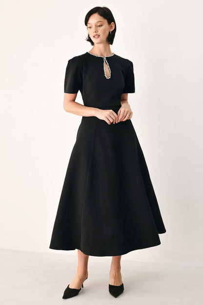 Full-length view of the black puff sleeve midi dress with a flared skirt, styled with black pointed-toe heels.