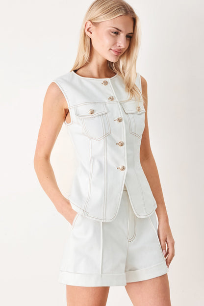 Woman wearing a white denim vest over a white dress on a plain background