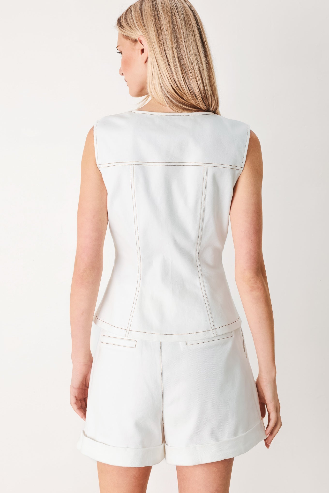 Woman wearing a light-colored sleeveless top and shorts on a plain background