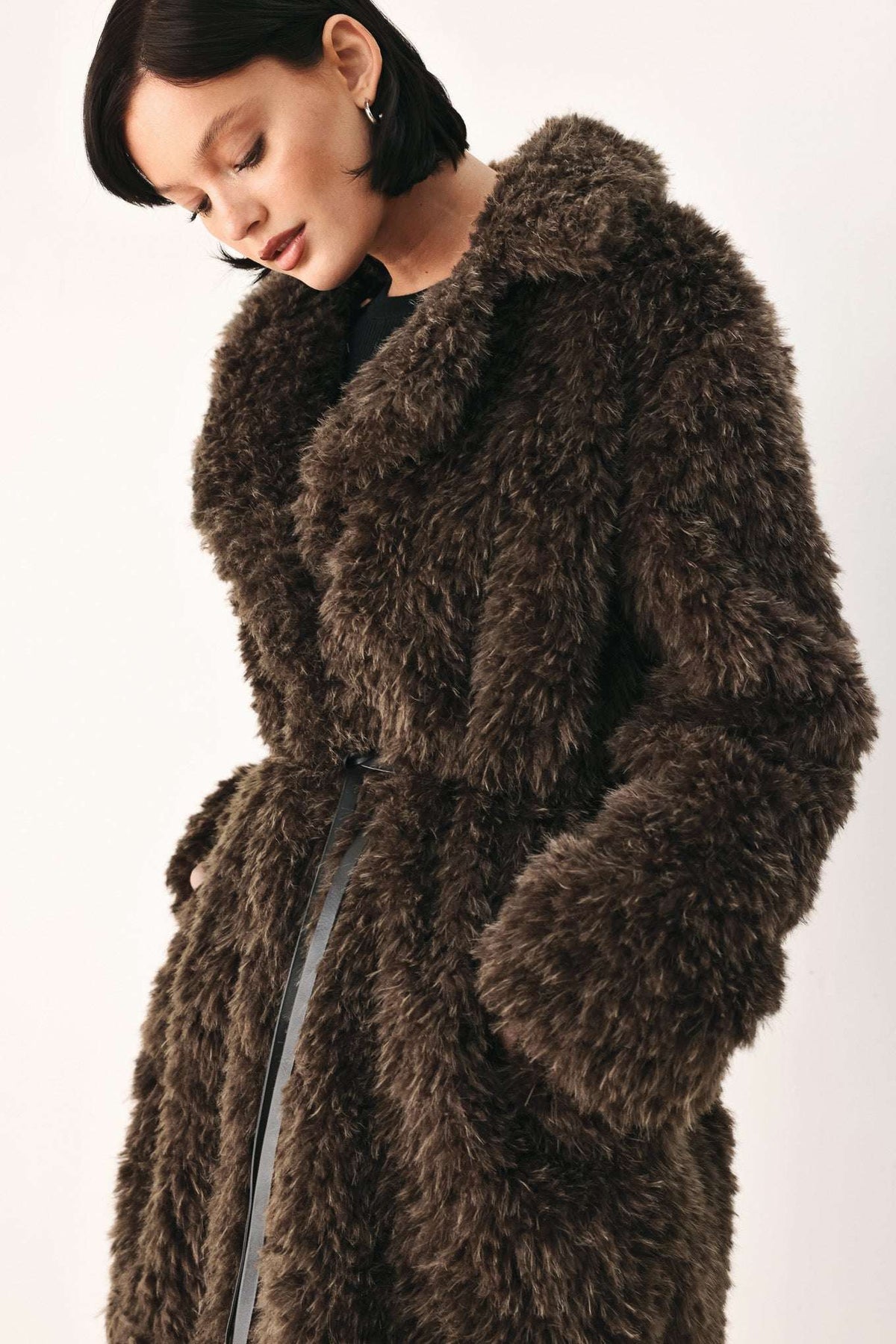 A model wearing a dark brown shaggy faux fur coat with a matching belt, photographed against a plain light background.