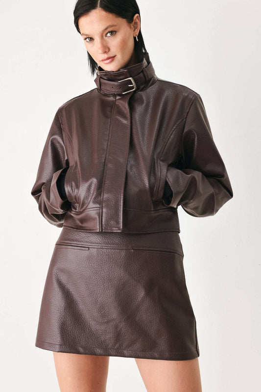A model wearing a dark brown faux-leather jacket and matching mini skirt against a plain light background.