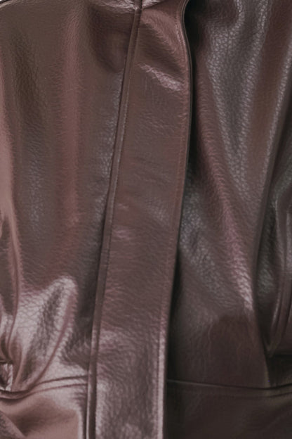 Close-up of a dark brown textured leather garment, showing the pebbled leather surface and a central seam.