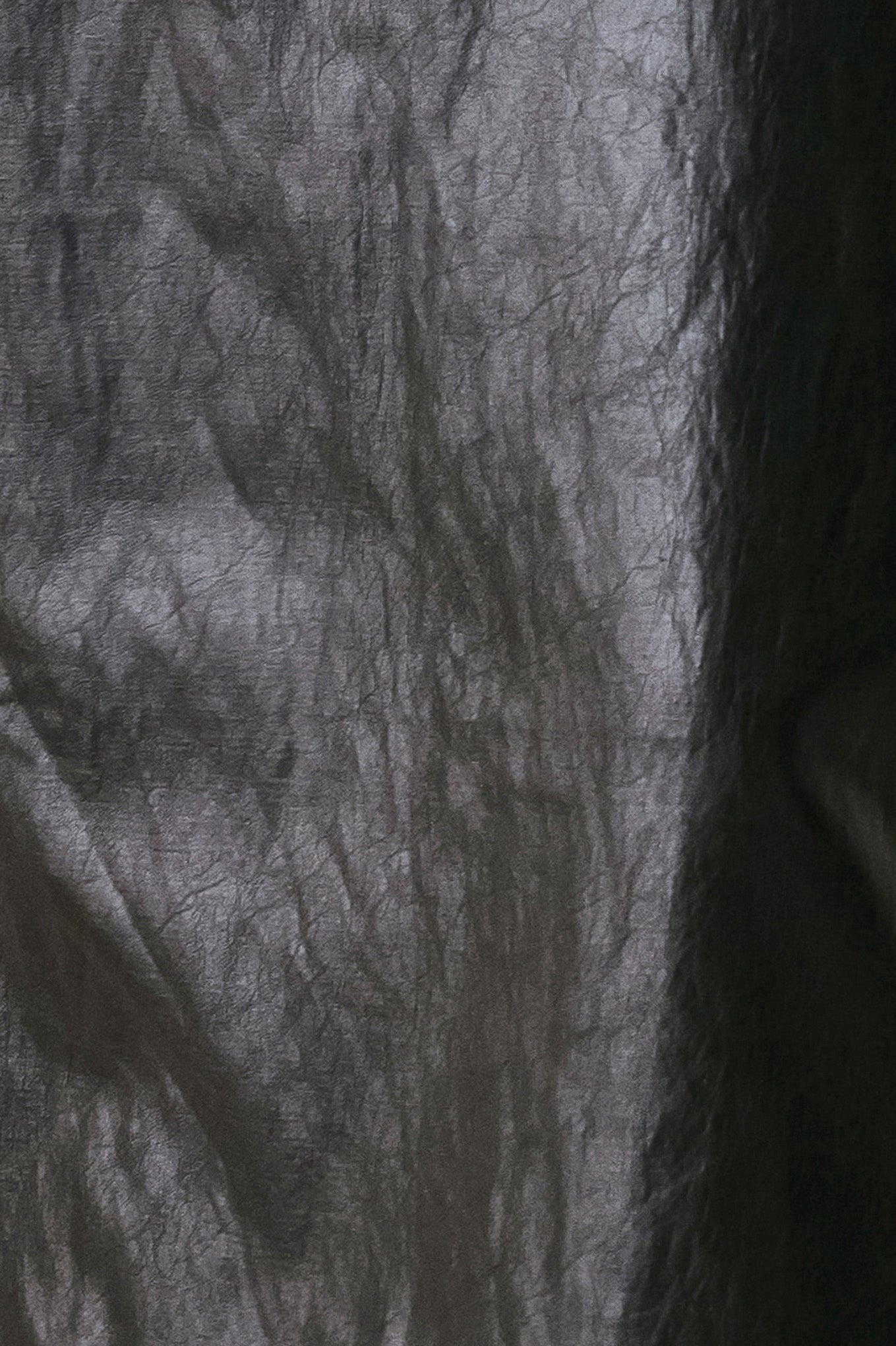 A close-up of a dark gray to black sheer mesh or netted fabric with a crinkled texture, filling the frame.