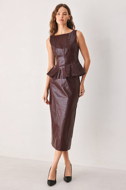 A woman modeling a dark brown faux-leather two-piece set consisting of a sleeveless peplum top and a matching pencil skirt, paired with black heels, against a plain light gray studio background.