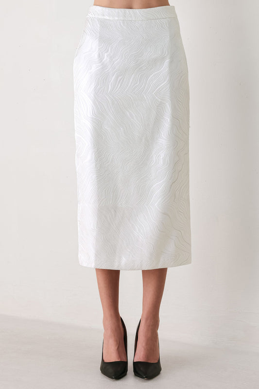 A white midi skirt with a subtle textured, wavy jacquard pattern, shown on a model wearing black pointed-toe heels against a plain off-white studio background.