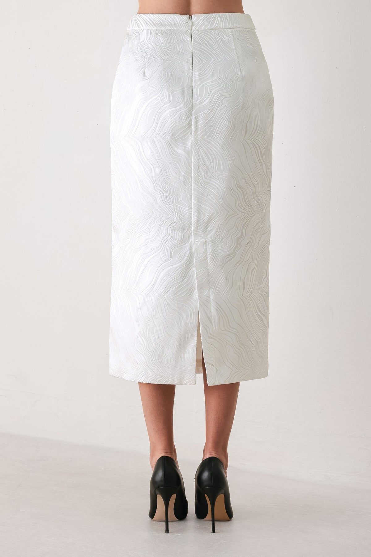 A white textured midi skirt with a front slit, shown from the back on a model wearing black high heels against a plain light background.