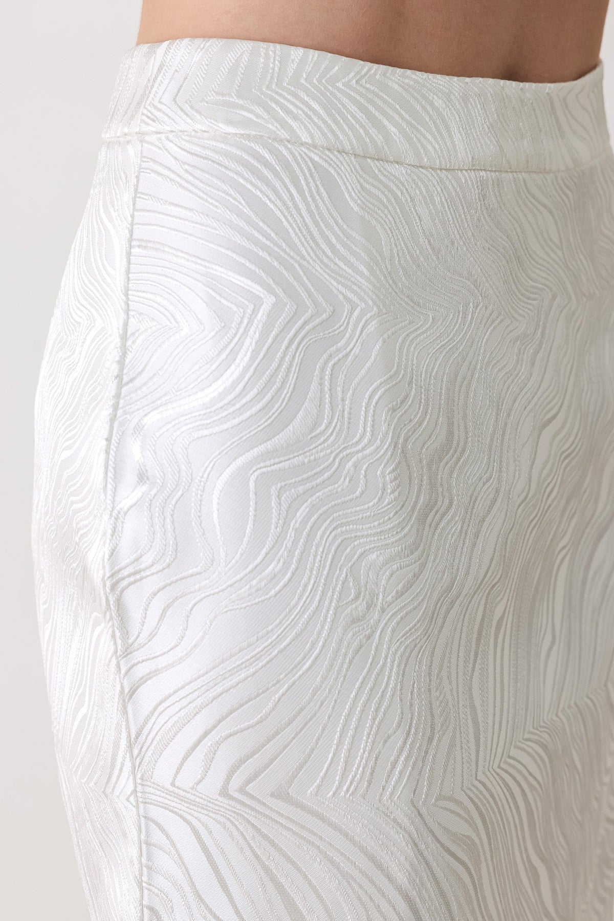 Close-up of a white textured skirt with a wavy, embossed pattern, shown on a model against a light background.