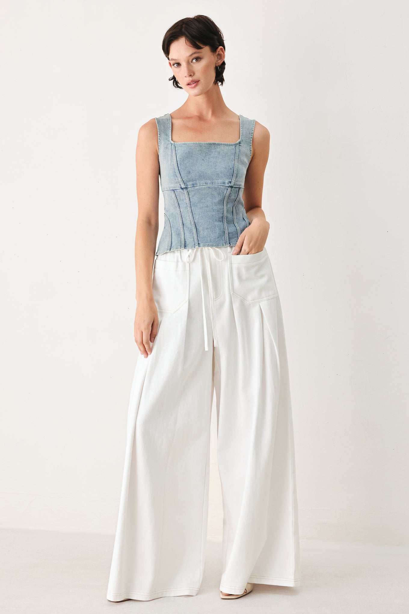 Woman wearing a blue top and white pants on a white background