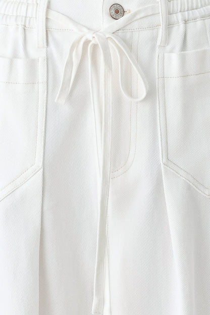 Close-up of white pants with a button and drawstring on a white background