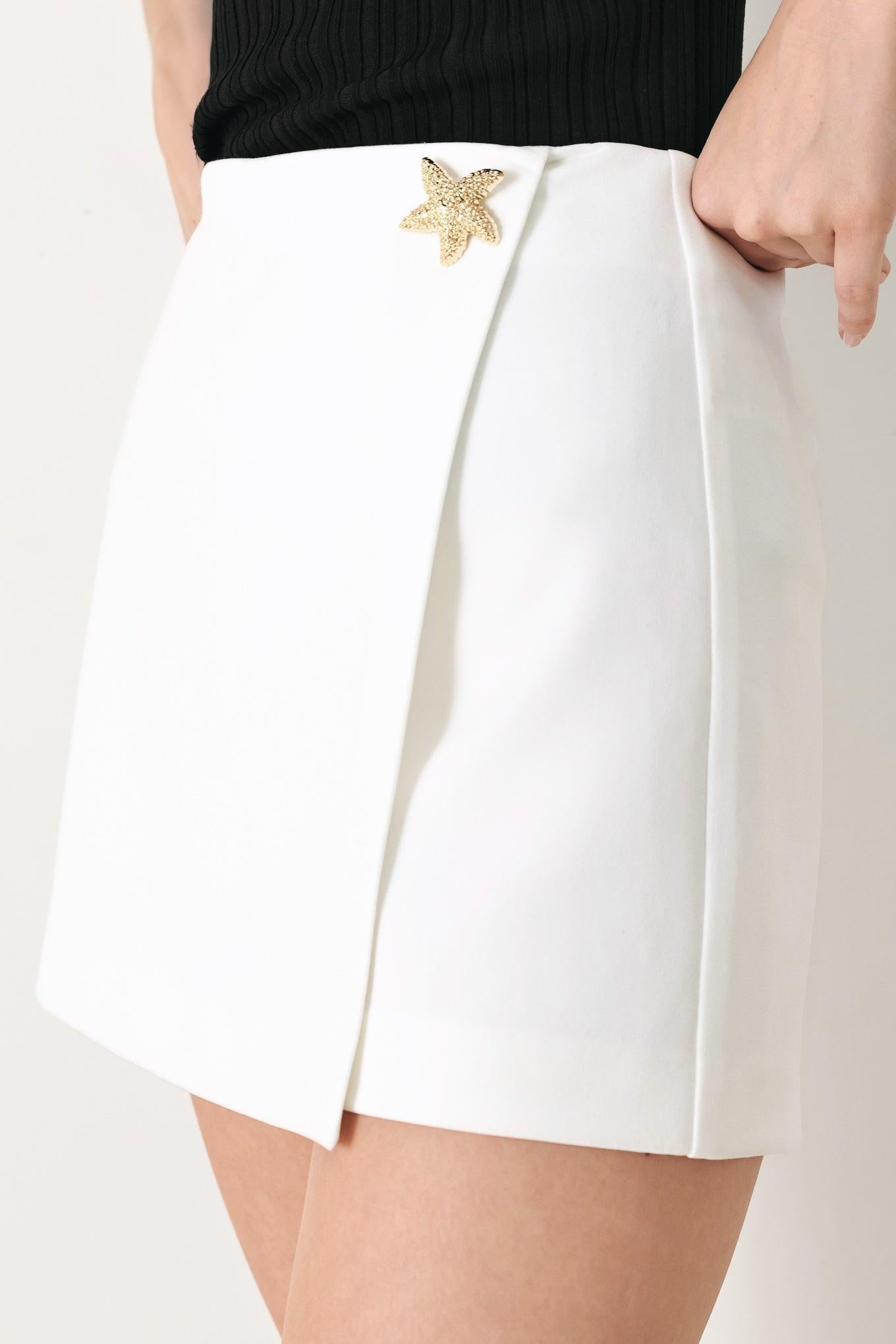 White shorts with a gold starfish accessory on a plain background