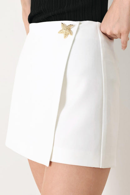 White shorts with a gold starfish accessory on a plain background