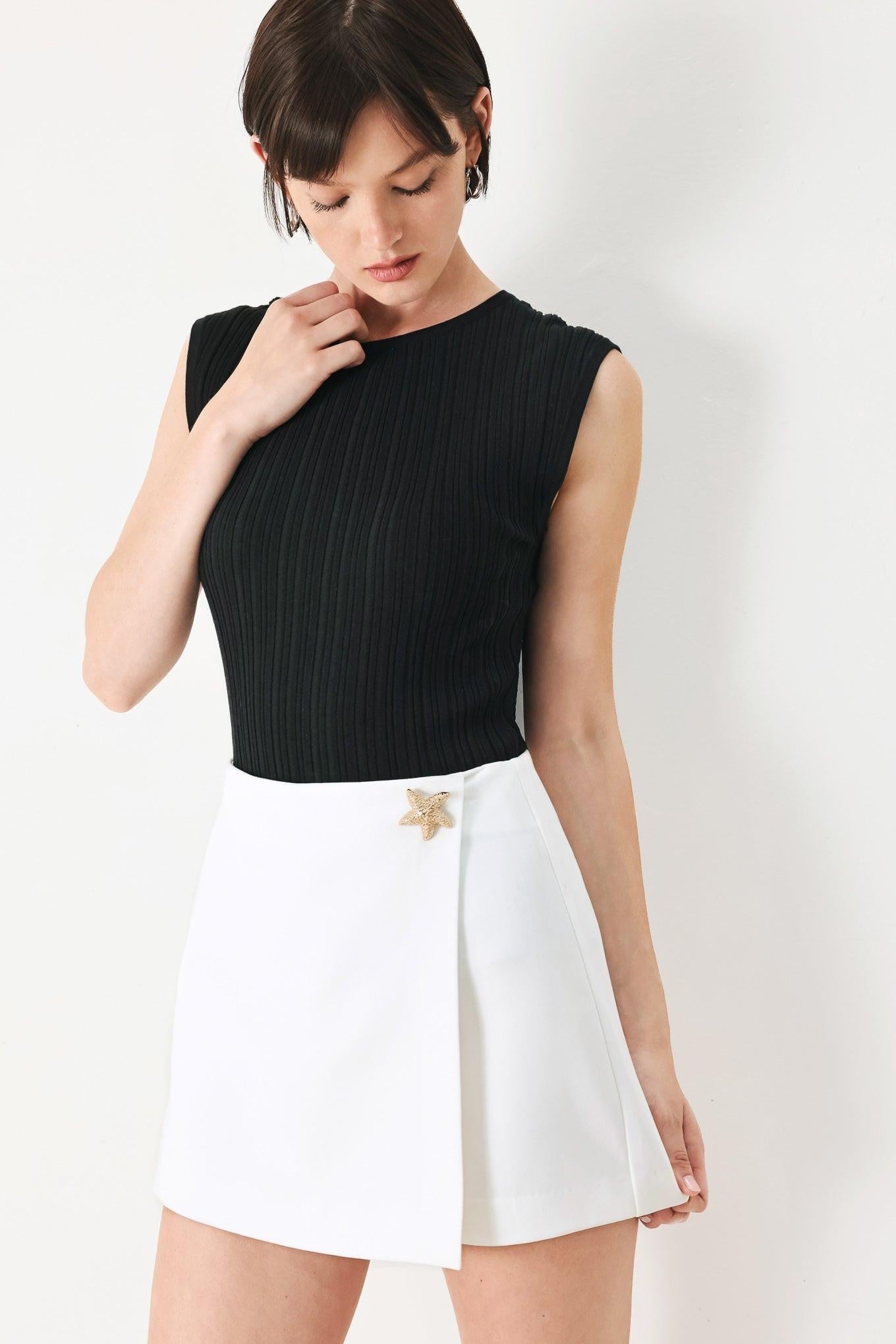 Woman wearing a black sleeveless top and white skirt on a white background