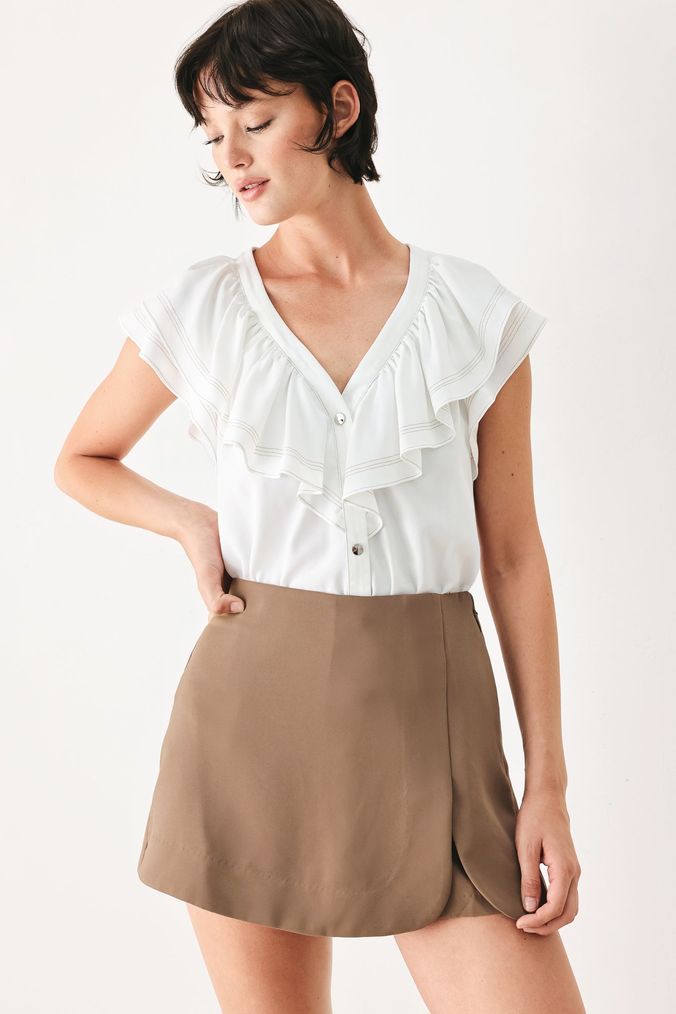 Woman wearing a white blouse with ruffled details and a brown skirt on a white background