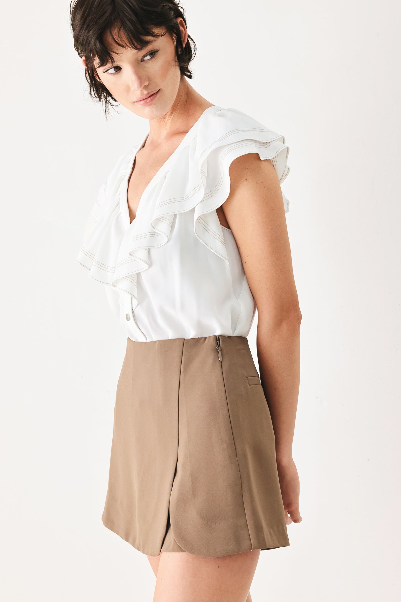 Woman wearing a white blouse with ruffled sleeves and a beige skirt on a white background