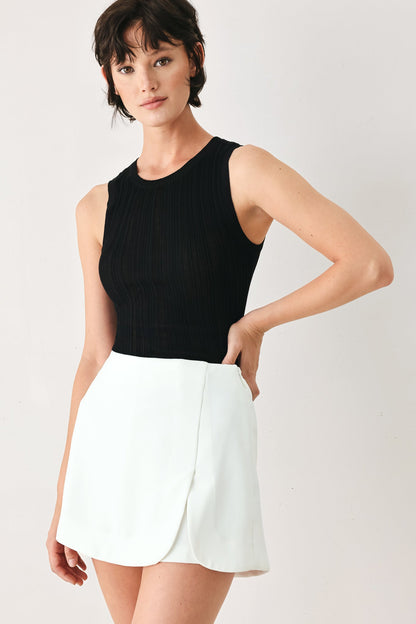 Woman wearing a black sleeveless top and white skirt on a plain background