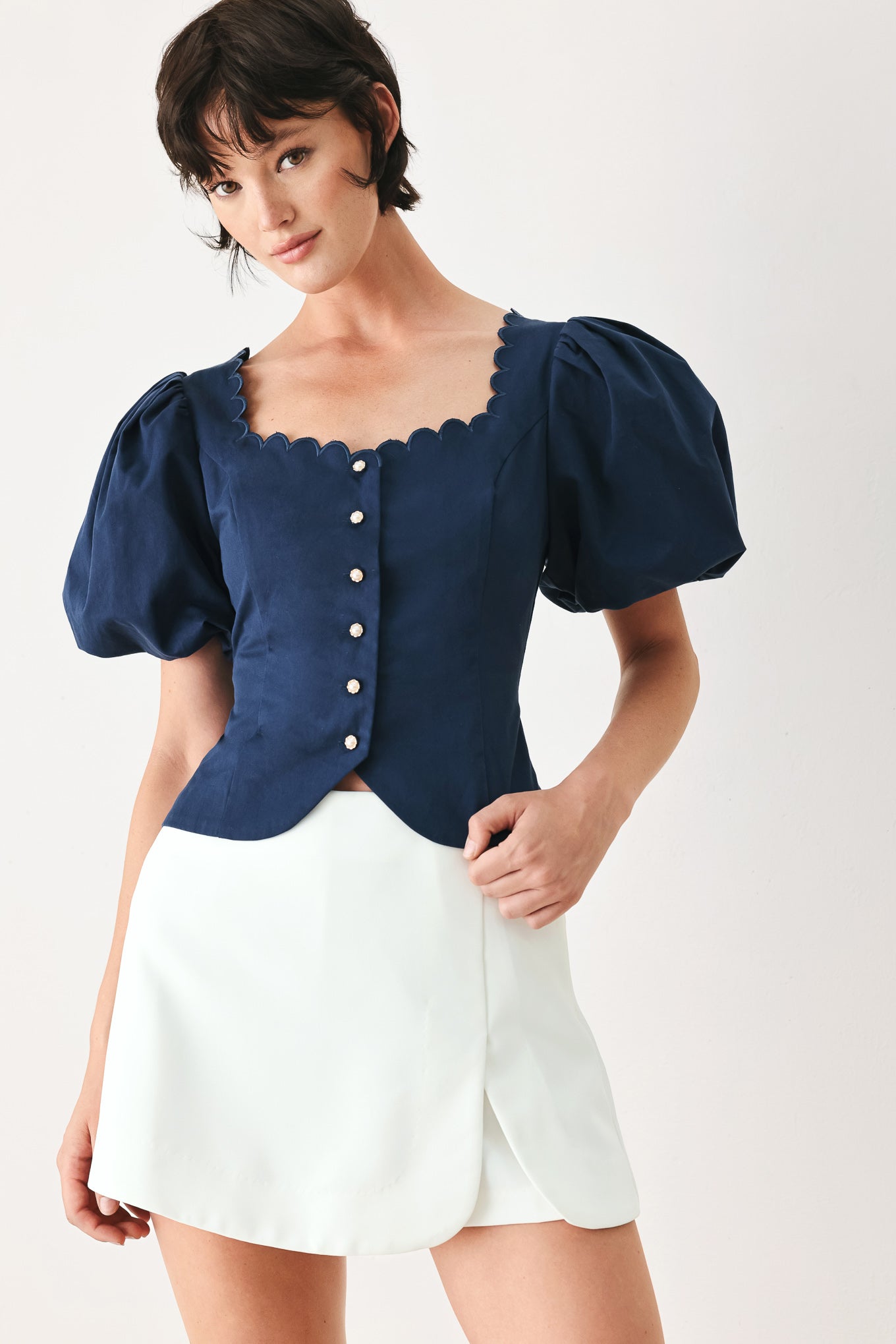 Woman wearing a blue blouse with puffed sleeves and a white skirt on a white background