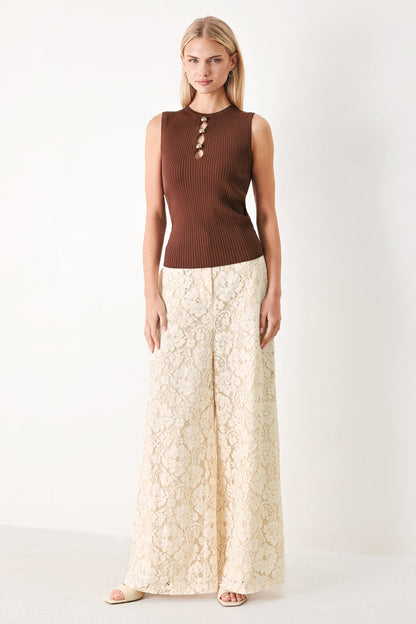 Woman wearing a brown sleeveless top and beige lace skirt on a white background