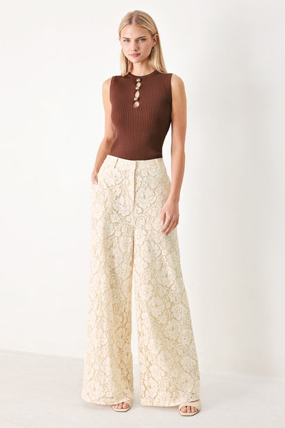 Woman wearing a brown sleeveless top and white lace pants on a white background