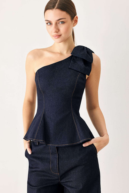 Dark blue denim one-shoulder top with a large bow on the strap and a flared peplum waist.