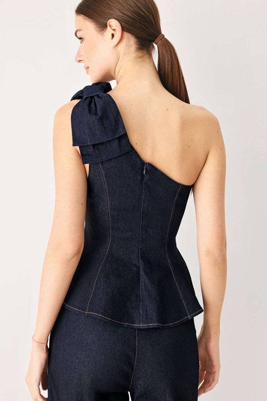 Rear view of a dark indigo denim one-shoulder top featuring a large bow on the shoulder and a back zipper.