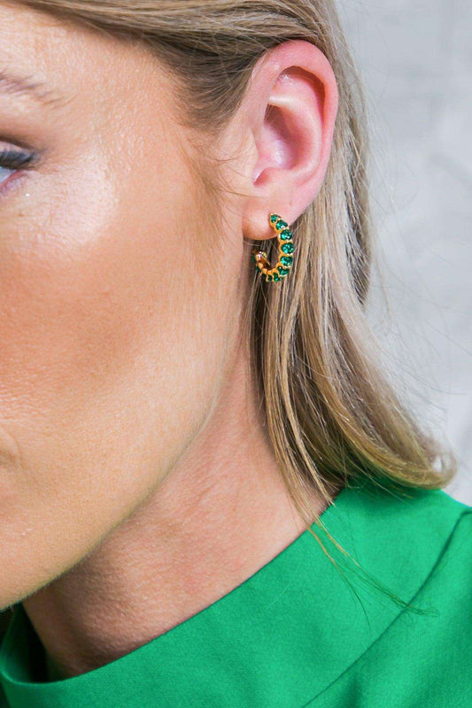 A person wearing a gold-toned hoop earring set with round green stones.