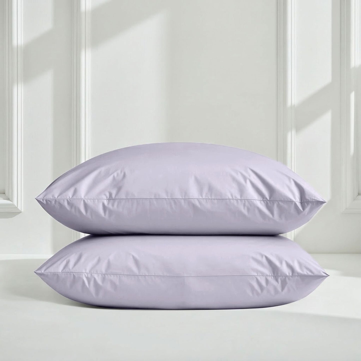 Two lavender pillows on a white surface with a light gray wall background