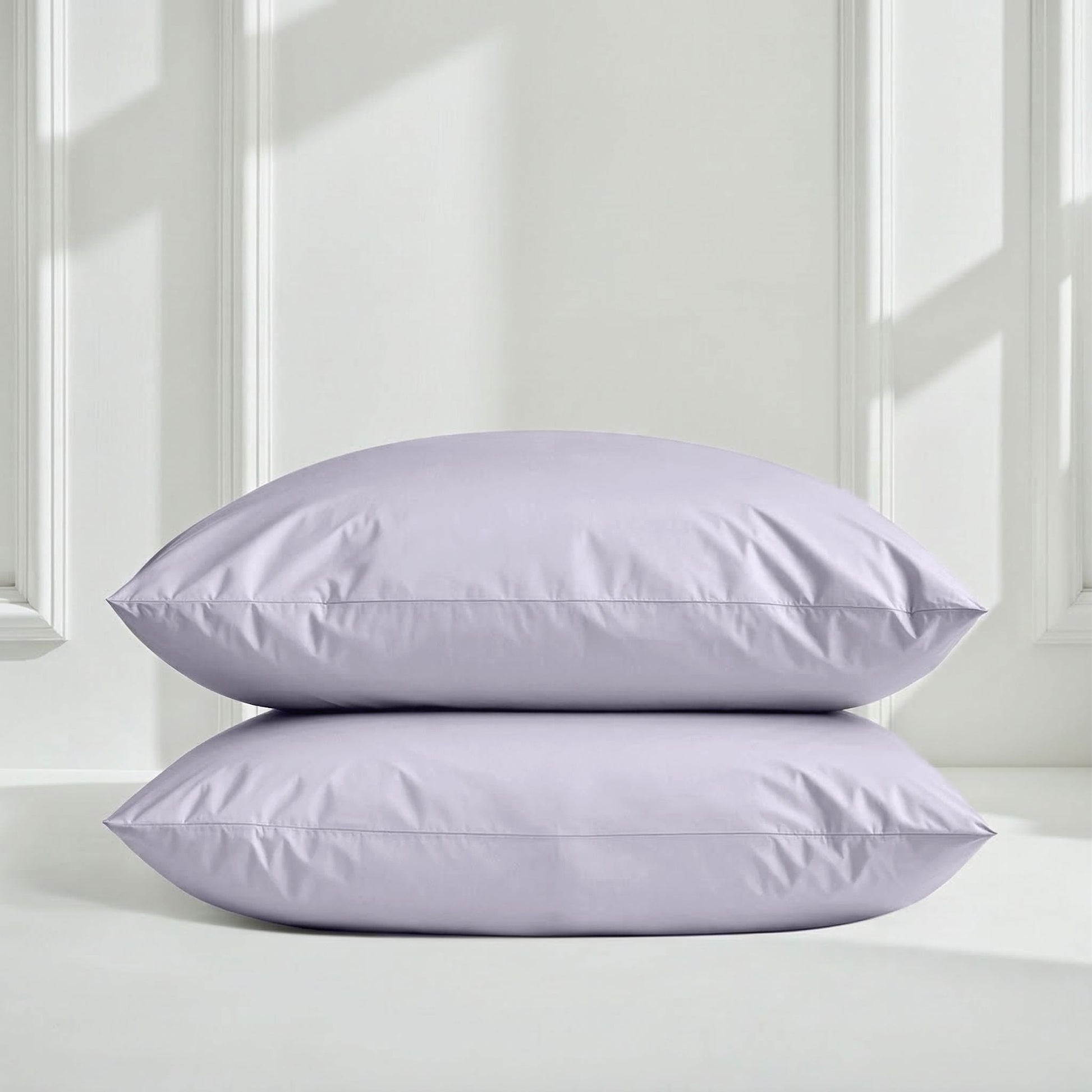 Two lavender pillows on a white surface with a light gray wall background