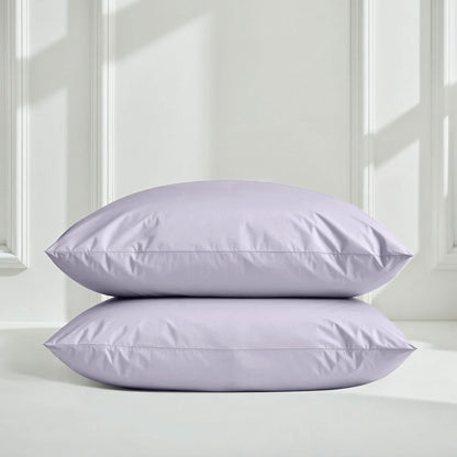 Two lavender pillows on a white surface with a light gray wall background