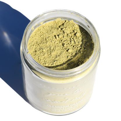 Jar of green powder with a blue background