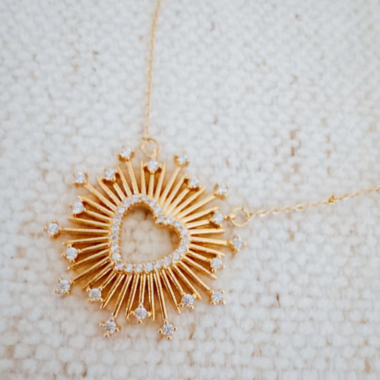 Gold necklace with a heart-shaped pendant on a textured beige background