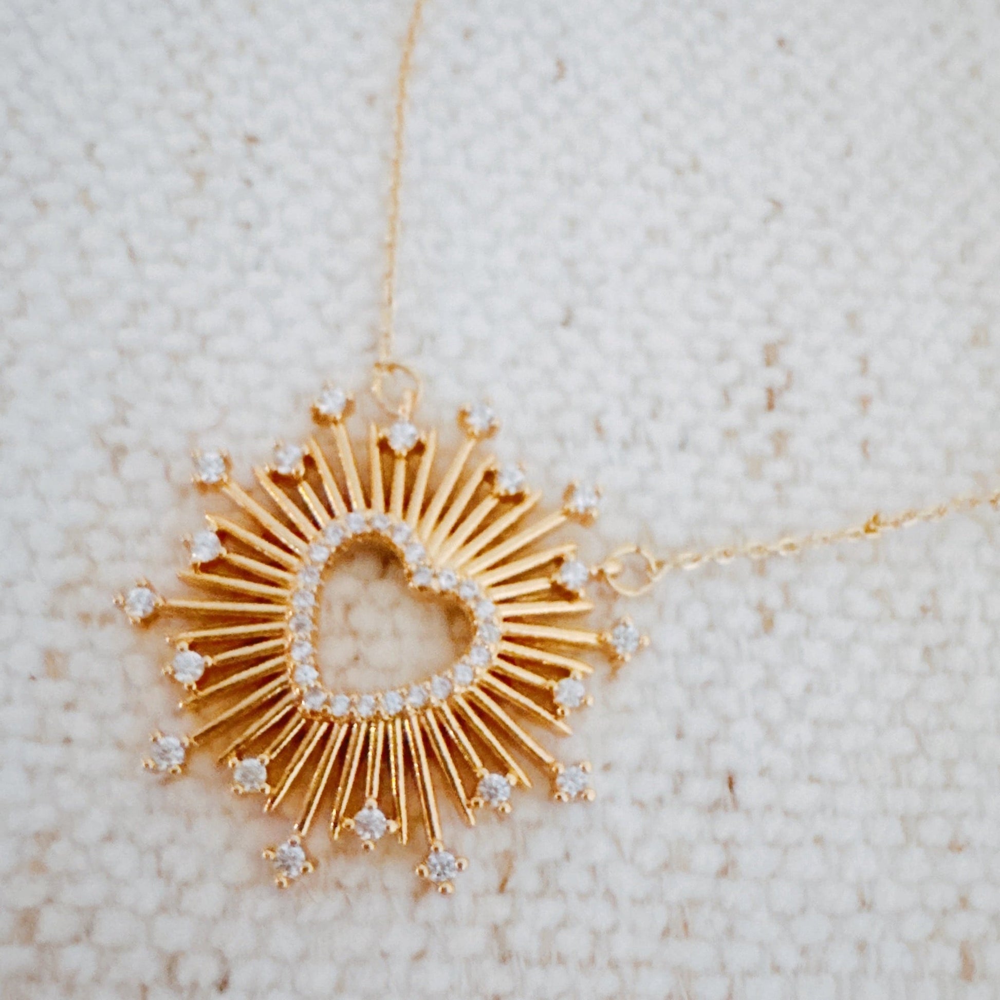 Gold necklace with a heart-shaped pendant on a textured beige background