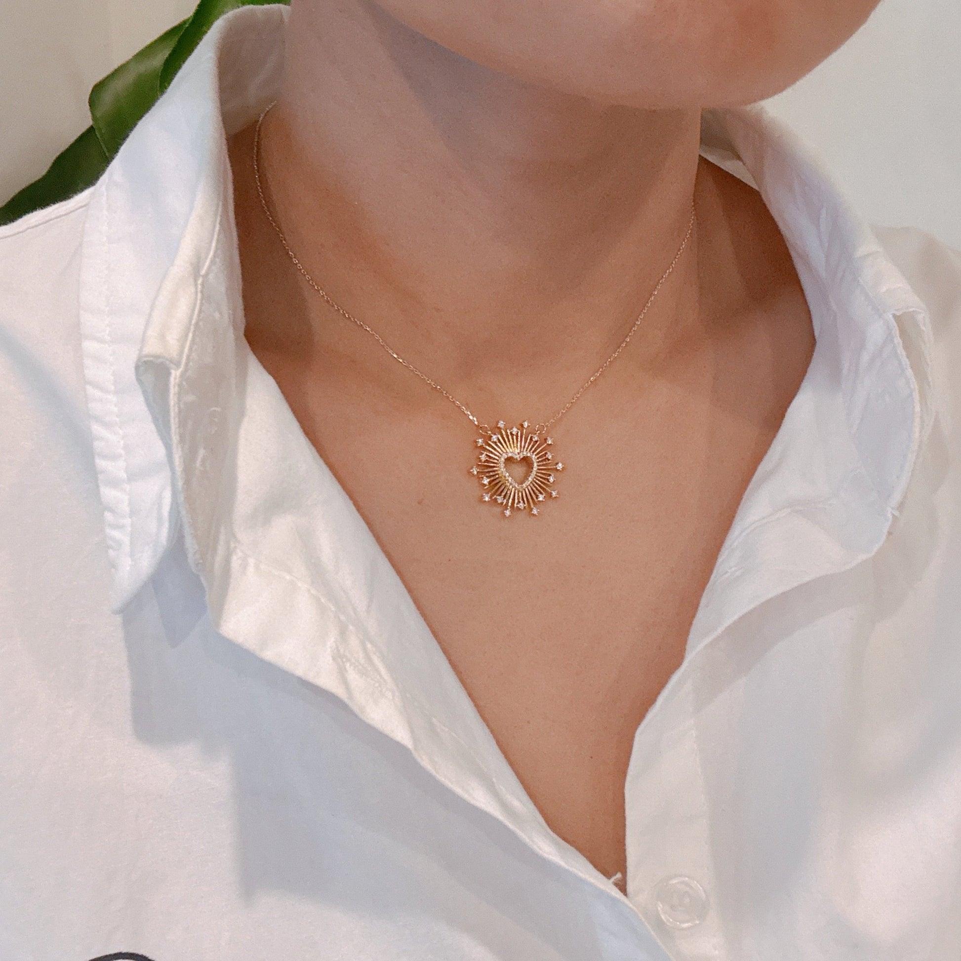Gold necklace with a heart design worn by a person in a white shirt.